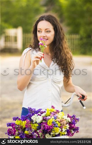 A beautiful young woman with her bicycle smelling wildflowers