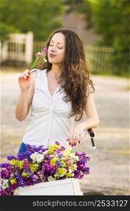 A beautiful young woman with her bicycle smelling wildflowers