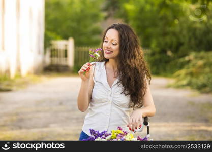 A beautiful young woman with her bicycle smelling wildflowers