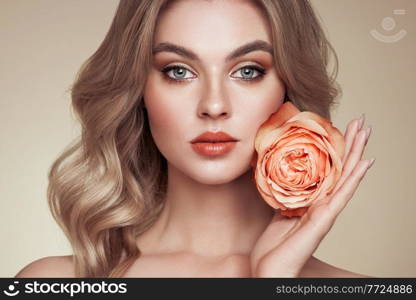 A beautiful young woman with shiny wavy blonde hair. Model with healthy skin, close up portrait. Girl with a rose flower