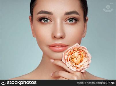 A beautiful young woman with shiny wavy blonde hair. Girl with a pink flower. Model with healthy skin. Cosmetology, beauty and spa
