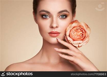 A beautiful young woman with shiny wavy blonde hair. Girl with a rose flower. Model with healthy skin. Cosmetology, beauty and spa