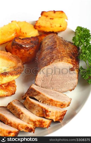 A beef &acute;eye roast&acute; joint, sliced into medallions, on a plate with roast potatoes and Yorkshire puddings.