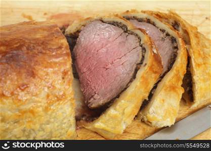 A beef wellington, or Boeuf en croute, sliced on a wooden chopping board, with a carving knife