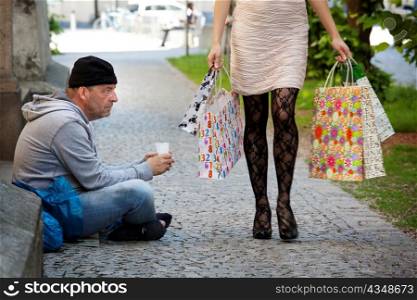 a beggar and a rich woman with shopping bags while shopping