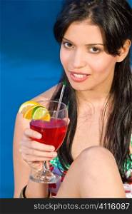 A beuatiful young Hispanic woman enjoying a cocktail by her swimming pool