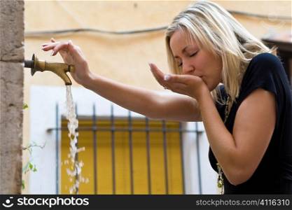 A beutiful young blond woman drinking from an outside tap