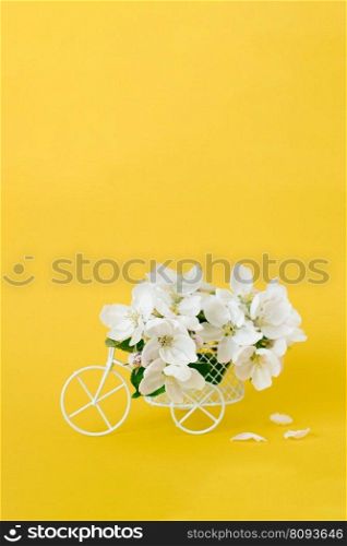 A bicycle toy with white flowers on a yellow background. The concept of celebration, banner. Copy space. The beginning of spring and the holiday