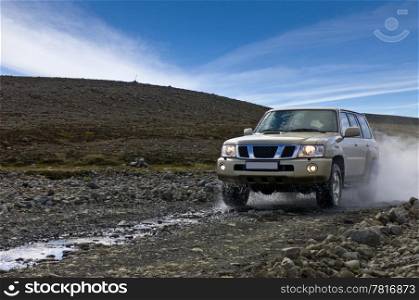 A big four by four car, emerging from a river, driving off over the uneven dirt road in Iceland