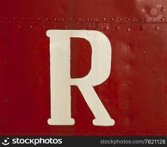 A big white letter &rsquo;R&rsquo;, part of a ship&rsquo;s name, surrounded by a sea of intense red paint on the metal hull of the boat.