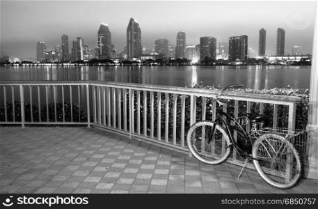 A bike is locked to the fence in Coronado with San Diego in the background at night