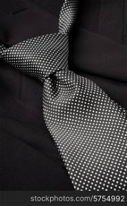 A black and white dotted tie, already with a knot, lying loosely on a dark suit.