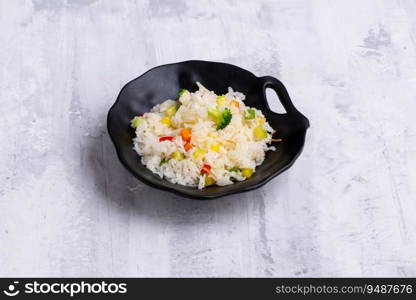 A black bowl of rise with vegetables isolated on a grey wooden background. Black bowl of rise with vegetables isolated on a grey wooden background