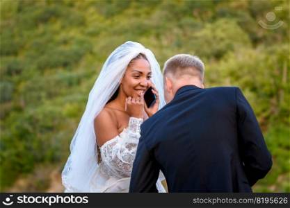 A black bride accepts congratulations on the phone and looks happily at her white husband