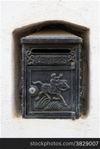 A black cast iron letterbox in a white wall niche with an engraving of a horse and knight and the word LETTERS.