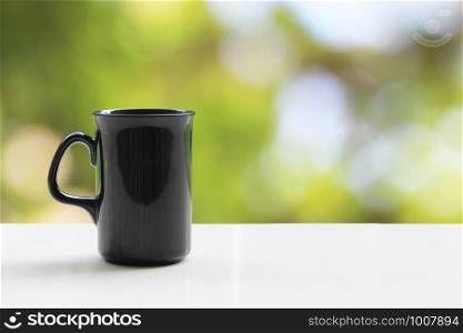 A black coffee mug on a white table On a natural background.