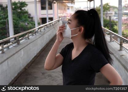 A Black shirt woman standing on putting on a respirator N95 mask to protect from airborne respiratory diseases as the flu covid-19 coronavirus PM2.5 dust and smog on the road burred background