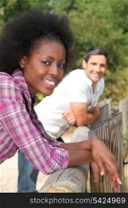 a black woman and a man leaning against wooden barrier