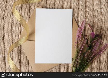 A blank card is placed on an envelope with a ribbon, flowers and a sweater.