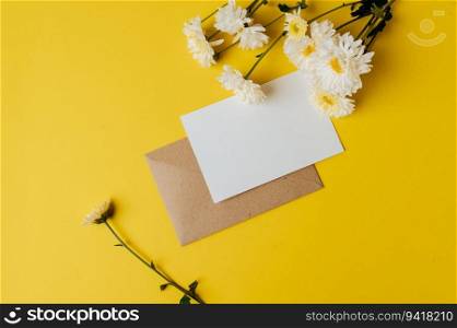 A blank card with envelope and flower is placed on yellow background