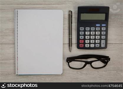 A blank notebook with a pencil and a calculator on a grey wooden background