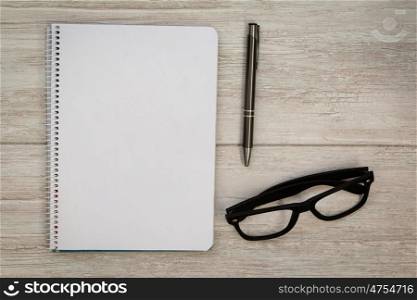 A blank notebook with a pencil and glasses on a grey wooden background