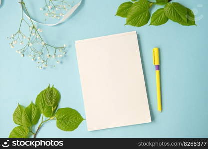 A blank sheet in a notebook, top view, a branch with leaves and a gypsophila on a bright blue table. Mockup . Space for text and copy space. A blank sheet in a notebook, top view, a branch with leaves and a gypsophile on the table