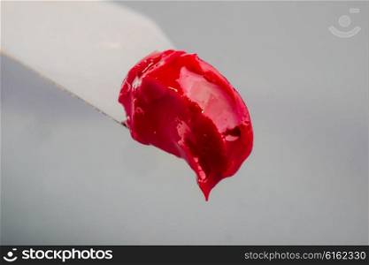 A blob of red oil paint, freshly squeezed from the tube and still wet sits on the tip of a scalpel as it is viewed up close.