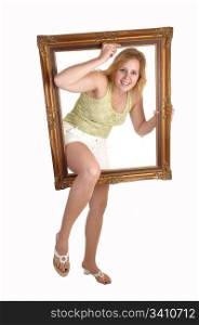 A blond a happy woman going with one leg and her body trough a pictureframe, in shorts and heels and green top for white background.
