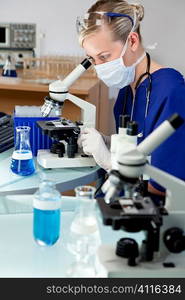 A blond female medical doctor or scientific researcher using her microscope in a laboratory.