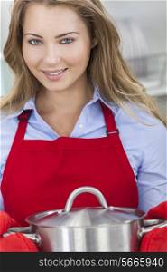 A blond girl or young woman looking happy wearing red apron &amp; cooking in her kitchen at home
