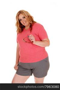 A blond plus size woman standing in shorts and a pink sweater,holding her sunglasses, isolated for white background.