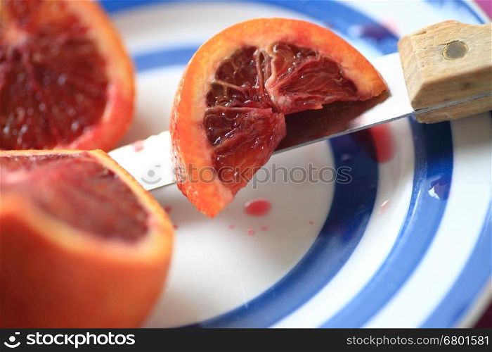 A blood orange with a section cut, resting on a knife on a blue-ringed dish