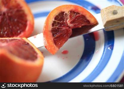 A blood orange with a section cut, resting on a knife on a blue-ringed dish
