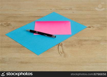 A blue paper and an a pink envelope with a black pen