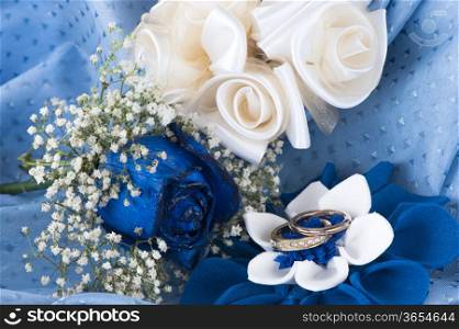 a blue roses and wedding rings on white background