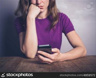 A bored young woman is using a smartphone at a table