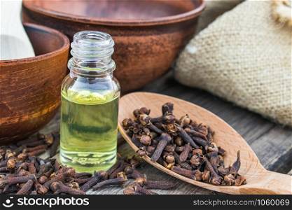 A bottle of clove essential oil stands near a spoon with clove spices on old wooden boards. Phytotherapy.. A bottle of clove essential oil stands near a spoon with clove spices on old wooden boards.