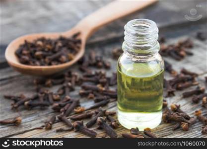 A bottle of clove essential oil stands near a spoon with clove spices on old wooden boards. Phytotherapy.. A bottle of clove essential oil stands near a spoon with clove spices on old wooden boards.