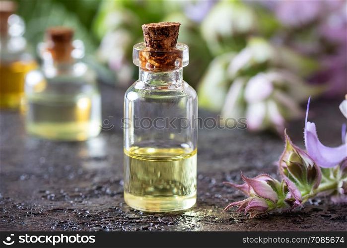A bottle of essential oil with blooming clary sage twigs on a dark background