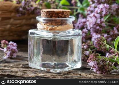 A bottle of essential oil with fresh blooming oregano twigs