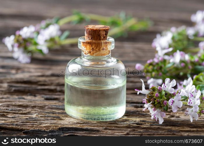 A bottle of essential oil with fresh blooming thyme on a rustic background