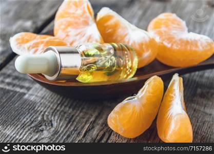 A bottle of mandarin essential oil and slices of ripe yellow mandarin lie on a wooden table. Citrus fruits, tangerines or oranges. Alternative medicine. A bottle of mandarin essential oil and slices of ripe yellow mandarin lie on a wooden table.