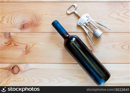 a bottle of red wine and a corkscrew on wooden boards top view close-up