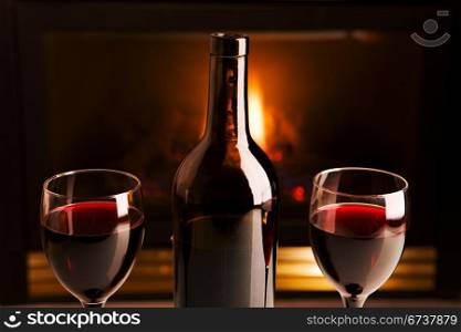 A bottle of red wine and two glasses in front of a fireplace