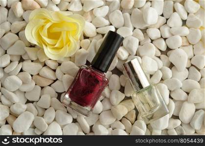 A bottle red and clear nail polish displayed on white pebbles with a white flower