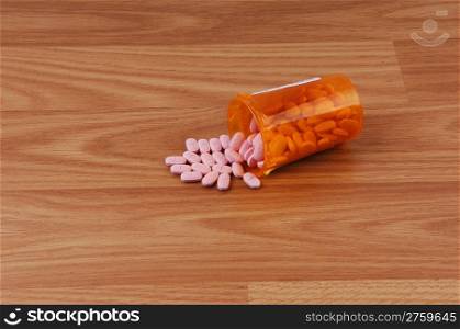 A bottle with orange pills spill out on a wood background.