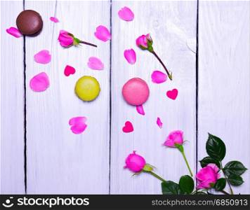 A bouquet of blooming pink roses and three multicolored macaroons on a white wooden background. blooming pink roses and three macaroons