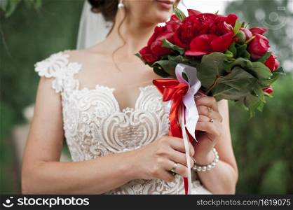 A bouquet of red peonies in the hands of a bride in a wedding dress.. A beautifl bouquet of bright red peonies in the hands of a girl 2848.