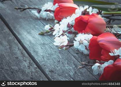 A bouquet of red tulips and white flowers on a background of wooden, old boards. Place for text. The concept of spring has come. View from above. Banner March 8, Easter. A bouquet of red tulips and white flowers on a background of wooden, old boards. Place for text. The concept of spring has come.